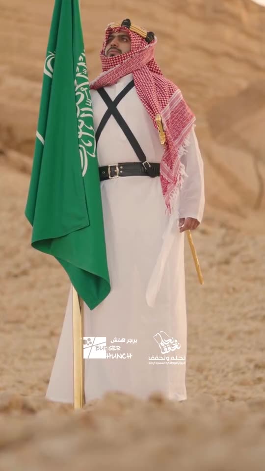 رجل يحمل علم المملكة في الصحراء